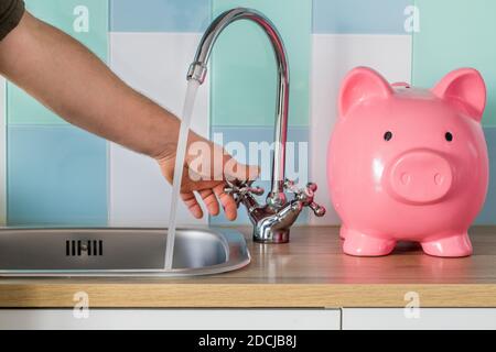 Flowing tap water and a piggy bank standing next to it. Water consumption price concept Stock Photo