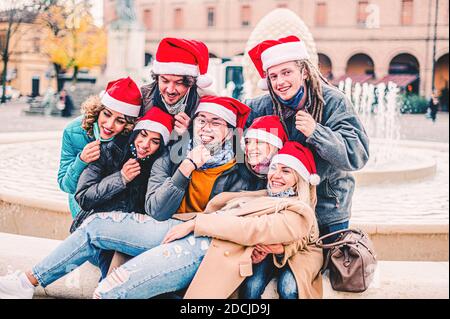 Multiracial team taking selfie wearing face mask and santa hat - New normal Christmas holiday concept with happy friends smiling together outside - Fo Stock Photo