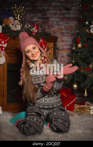 Cute young girl in a suit with deer on the background of a Christmas tree, puts on woolen gloves Stock Photo