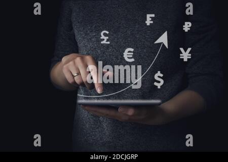 Hand holding tablet with a rising arrow and currency icons different countries. Business development to success and growing growth concept in 2021. Co Stock Photo