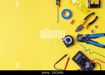 Different electrician's supplies on yellow background. Background of professional electrician tools with space for text Stock Photo