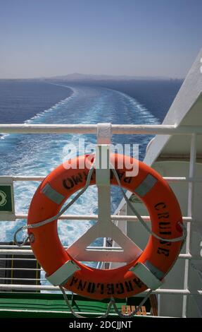 A lifebuoy hanging on the railing of a yacht or ship. The vessel leaves a white bubbling wake in its trail. Stock Photo