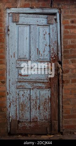 Blue door with peeled paint in a brick wall Stock Photo