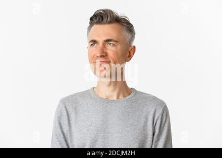 Close-up of disappointed middle-aged man in gray sweater, frowning upset and looking left at copy space, standing over white background Stock Photo