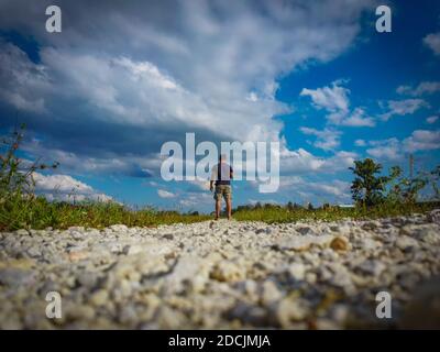 Single man standing in the gravel pathway in the field, preparing to launch his drone into air, photographed from back Stock Photo