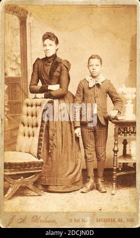 Unidentified standing figures: woman, her folded arms leaning on back of chair, and young man, probably her son, left hand on book., still image, Photographs, 1890, Wilson, J. A Stock Photo