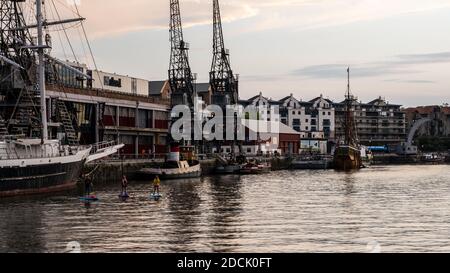 Three people paddleboard outside M Shed on Bristol's Floating Harbour docks on a late summer evening. Stock Photo