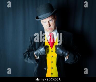 Portrait of Mean Looking Man in Bright Yellow Waistcoat and Leather Gloves. Concept of Comic Book Henchman. Dark Criminal Villain. Stock Photo