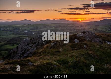 The sunset casts a red sky over the mountains of Yr Eifl and Bwlch Mawr on the Lleyn Peninsula in north Wales, viewed from Moel-y-Gest in Snowdonia Na Stock Photo