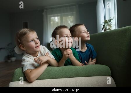 Beautiful children lie on the sofa at home, looking to the side. Stock Photo