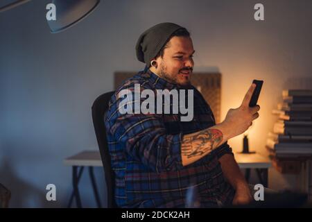 A closeup portrait of a smiling cute man with hat making video call on smartphone at home Stock Photo