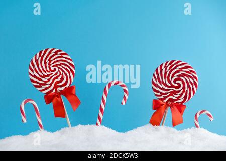Christmas red candy canes and lollipops in snow on blue background. Merry Christmas sweets and Happy New Year concept Stock Photo