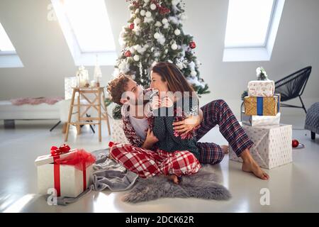 caucasian  guy hugging beautiful brunette in front of christmas tree beside pile of presents.christmastime Stock Photo