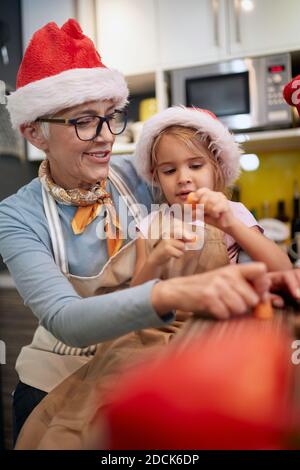 Grandma in a festive atmosphere getting help from granddaughter at the kitchen in preparation of Xmas meal. Christmas, family, together Stock Photo