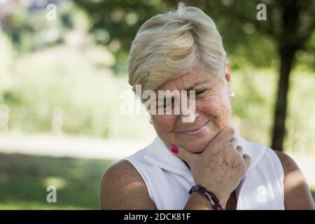 Portrait of sad senior woman in the park. Blonde hair mature lady crying outdoors. Bad news, loss, depressed, melancholy concepts Stock Photo