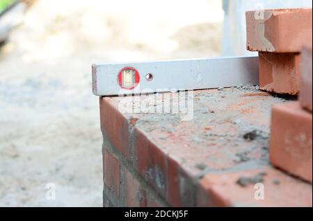 A close-up on a sprit level used to level the corner brick courses on a mortar bed while bricklaying the wall of the house. Stock Photo