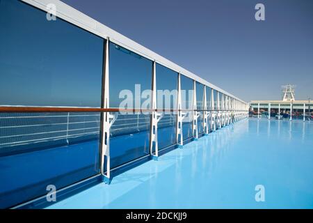 the deck of a ship in the summer sun. The fence in transparent panels in perspective and some travelers in the background Stock Photo