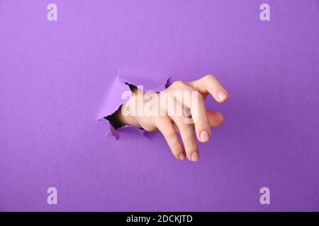 Hand is thrust through a hole in the paper background Stock Photo