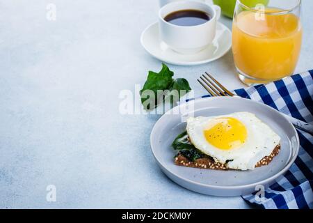 Rye bread toasts with fried spinach and egg with cup of coffee and orange juice on blue table background. Healthy Breakfast Food Concept. Copy Space Stock Photo