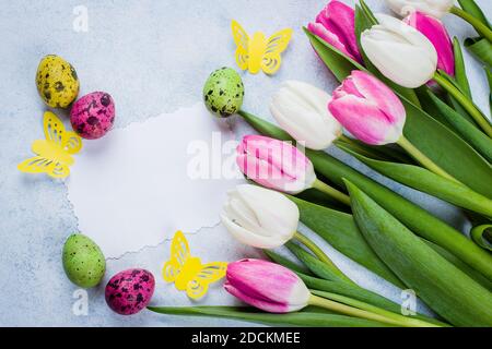 Spring Greeting card with empty paper blank. Easter Background with white and pink tulips and colorful quail eggs on blue stone table background. Top Stock Photo