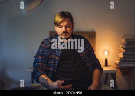 A closeup portrait of a serious attractive man using his smartphone while sitting at home Stock Photo