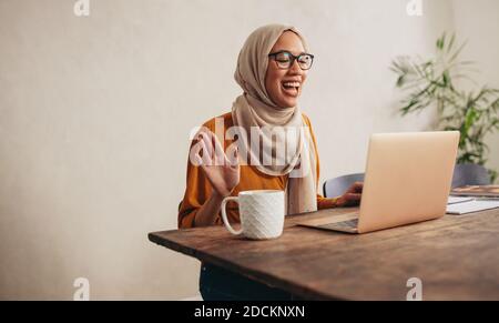 Muslim woman having a zoom meeting call on her laptop. Female working from home having a video conference, greeting to colleagues. Stock Photo