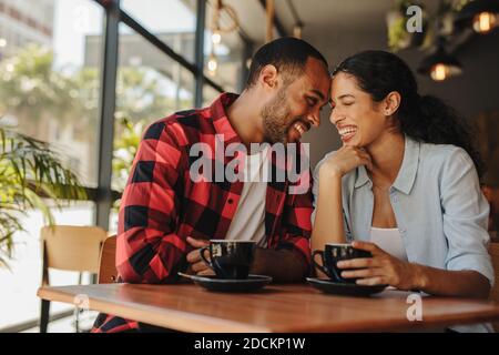 Loving couple enjoying their date at a local coffee shop. Smiling man and woman sitting at cafe touching their forehead. Stock Photo