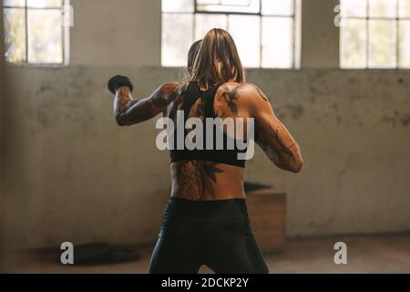 Woman in sportswear practicing shadow boxing at a fitness space inside abandoned warehouse. Tattooed female athlete doing shadow boxing workout inside Stock Photo