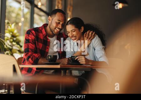 Smiling couple having fun sitting at a restaurant. Man and woman smiling with coffee cups on the table at cafe. Stock Photo