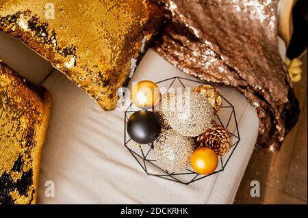 gold, beige and black glitter balls for Christmas decor in metal black basket on light sofa with gold shining pillows and blanket. holiday card, selec Stock Photo