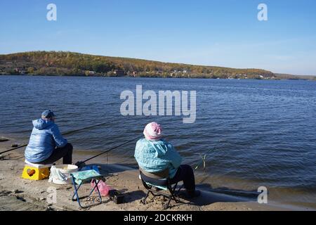 Two elderly people sit on the riverbank with fishing rods and fishing Stock Photo