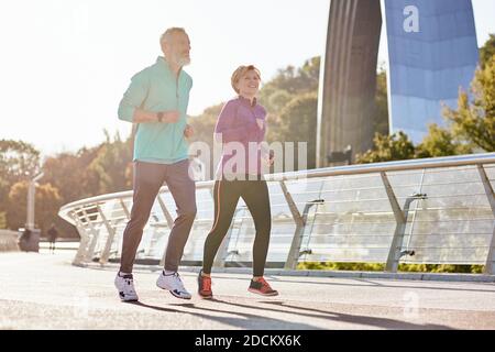 Healthy mind and body. Cheerful active mature couple in sportswear smiling while running on a sunny day. Joyful senior couple doing sport together Stock Photo