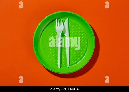 Plastic set of disposable tableware consisting of a plate, knife and fork on an orange background. Environmental concept. Ban single use plastic.Top v Stock Photo