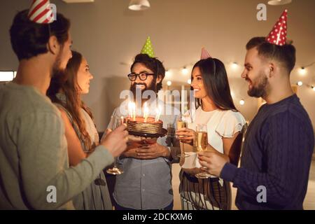 Group of people in cone party hats congratulate on the birthday of their happy friend. Stock Photo