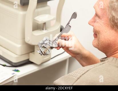 Senior man holding optometric trial frame for the selection of diopters. Ophthalmological clinic, vision examination. Stock Photo