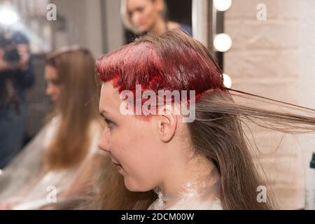 The girl’s half-colored head during hair coloring is reflected in the mirror in the hairdresser’s salon. Stock Photo