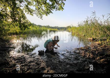 Happy child playing with dirty sand near the rural lake in summer day Stock Photo