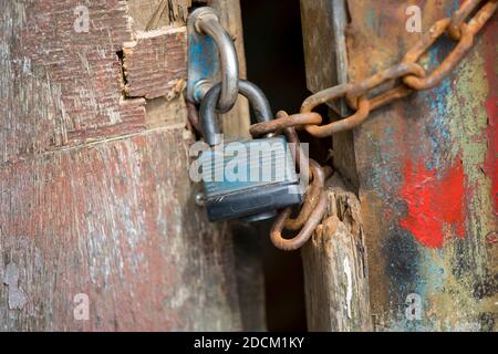 An old padlet that locks two doors of an old barn. The doors have red, blue and green paint on it and are rusty. Stock Photo