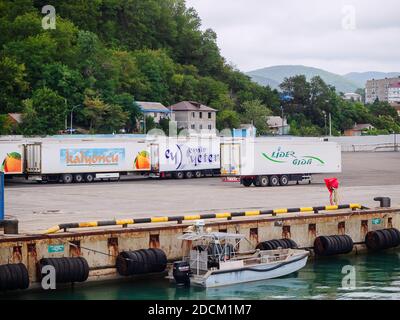 Russia, Tuapse 15.11.2020. Large white cargo vans with logos and lettering stand on the marina against the backdrop of green mountains Stock Photo