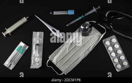 Surgical protection face mask, syringes, needles, test tube, digital thermometer, pills and stethoscope isolated on black background. Stock Photo