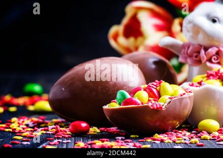 Easter composition: rabbit, chocolate eggs and sweets, red tulips and colorful sugar, selective focus Stock Photo