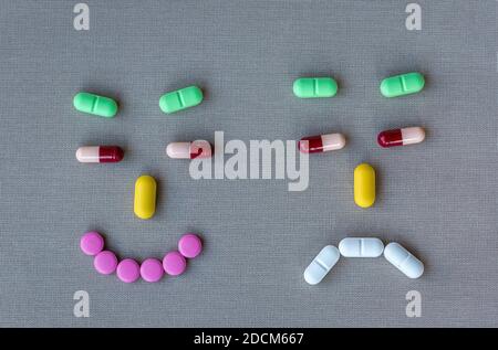 Funny faces made from different colorful pills. Smiling and sad face made of pills on gray textile background. Stock Photo