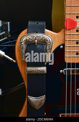 Electric guitar and leather strap with silver buckle. Close-up with glass slide, blues harp and cable jack. Stock Photo