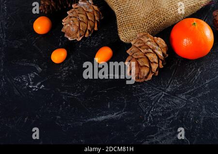 Christmas bag made of coarse burlap, cones, tangerines or oranges, kumquat on a dark background. Copy space. Stock Photo