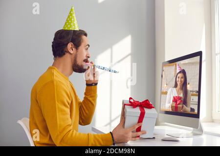 Happy young man sitting at computer and having virtual party with his friend or girlfriend Stock Photo
