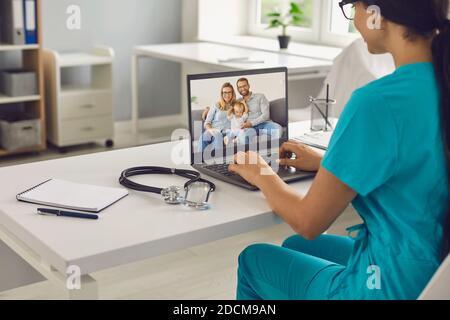 Female family doctor using laptop for online consultation with her patients while sitting in office. Stock Photo