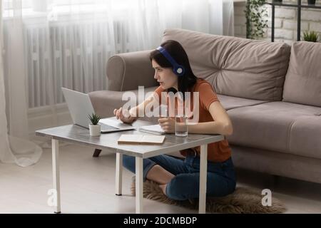 Focused young woman in headphones watching educational lecture on computer. Stock Photo