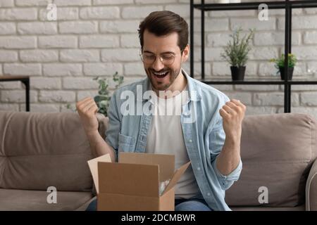 Happy young man in eyeglasses opening small cardboard parcel. Stock Photo