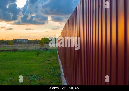 autumn sunset with dark dense clouds in the village, field with burgundy fence. Stock Photo