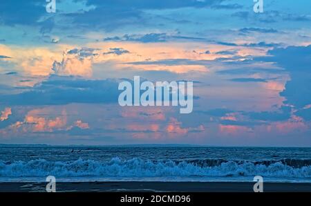 Colorful twilight view of layers of clouds over the ocean from Katase Higashihama Beach, with a lone surfer visible Stock Photo